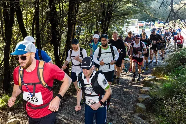 A group of people are running down a trail in the woods.