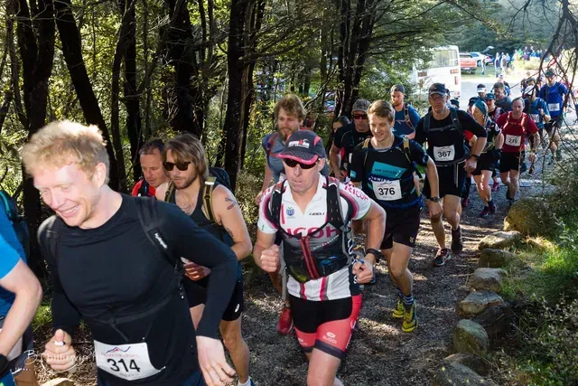A group of people are running down a trail in the woods.