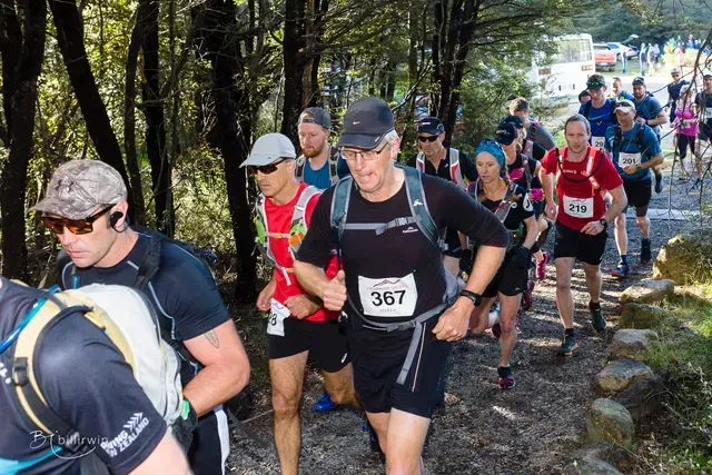 A group of people are running down a trail in the woods.