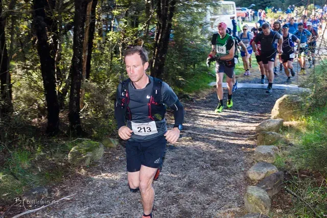 A group of people are running down a trail in the woods.