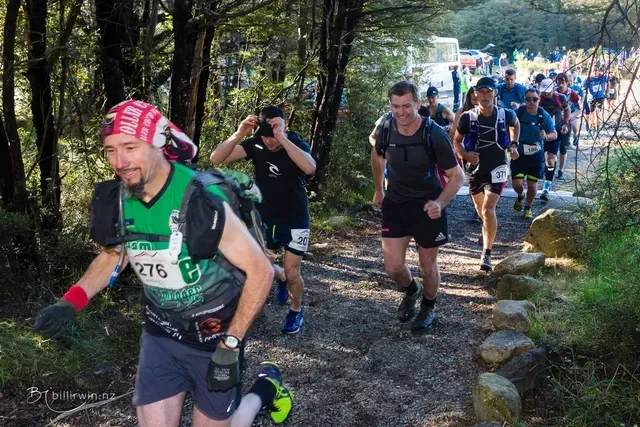 A group of people are running down a trail in the woods.