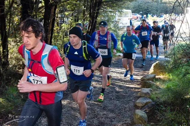 A group of people are running down a trail in the woods.