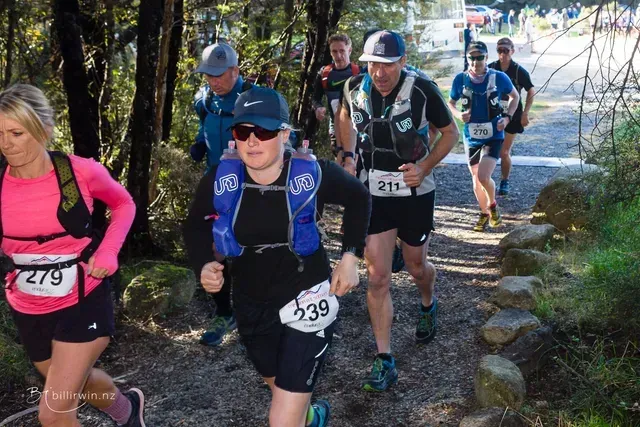 A group of people are running down a trail in the woods.