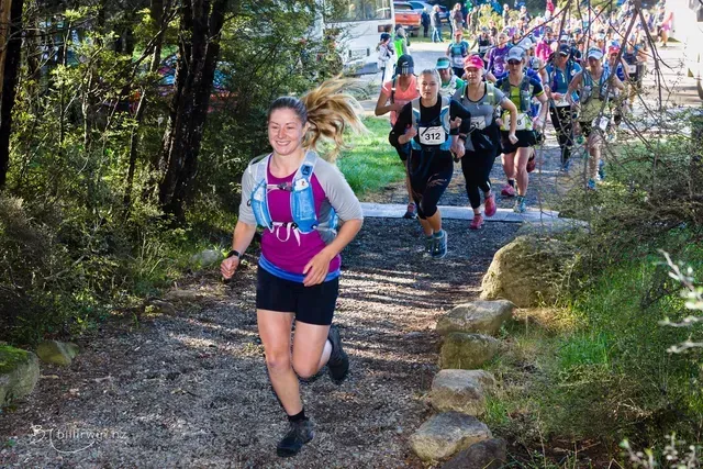 A group of people are running down a trail in the woods.