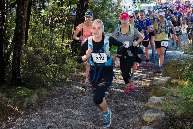 A group of people are running down a trail in the woods.