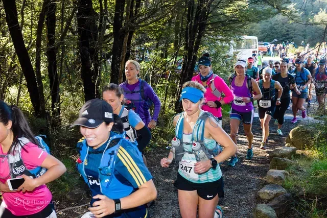 A group of people are running down a trail in the woods.