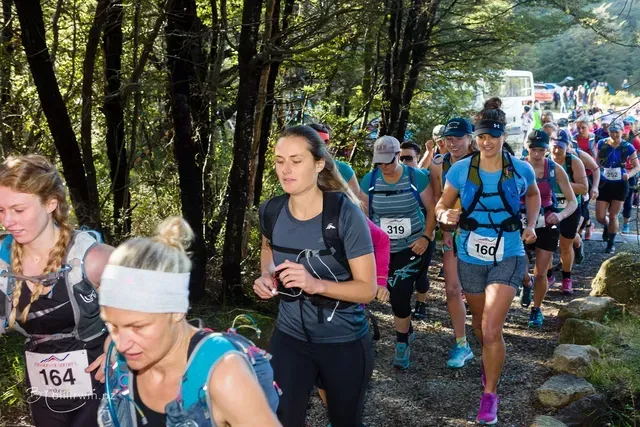A group of women are walking down a trail in the woods.