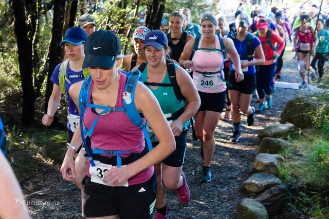 A group of women are running on a trail in the woods.
