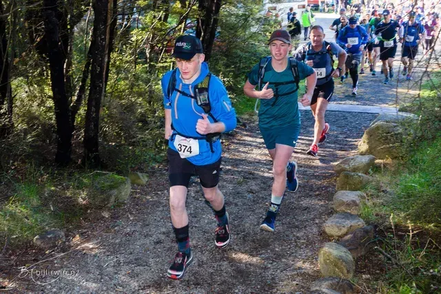 A group of people are running down a trail in the woods.