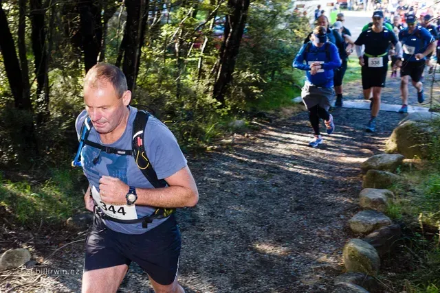 A group of people are running down a trail in the woods.
