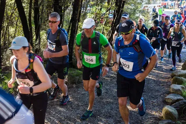 A group of people are running down a trail in the woods.