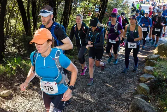 A group of people are running on a trail in the woods.