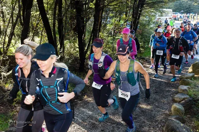 A group of people are running down a trail in the woods.
