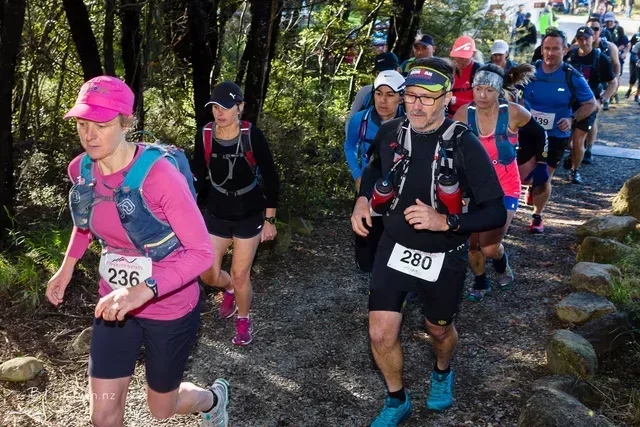 A group of people are running down a trail in the woods.