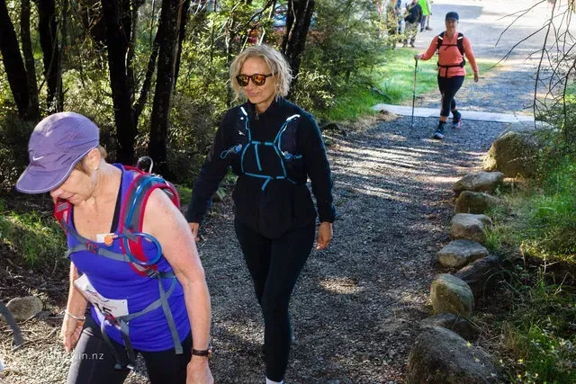 Two women are walking down a path in the woods.