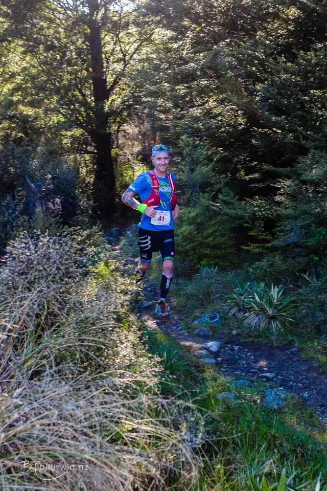 A man is running on a trail in the woods.