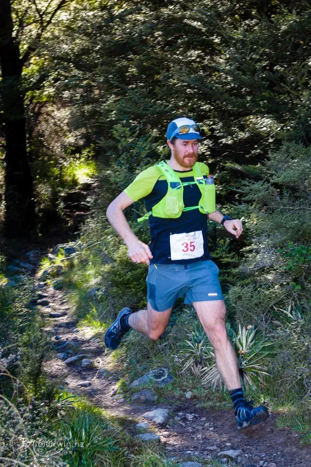 A man is running on a trail in the woods.