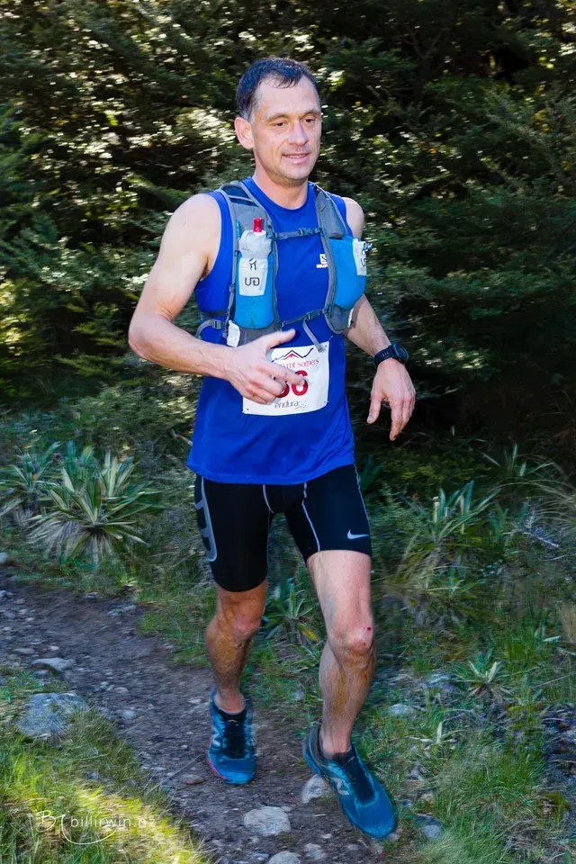 A man wearing a blue tank top and black shorts is running on a trail.