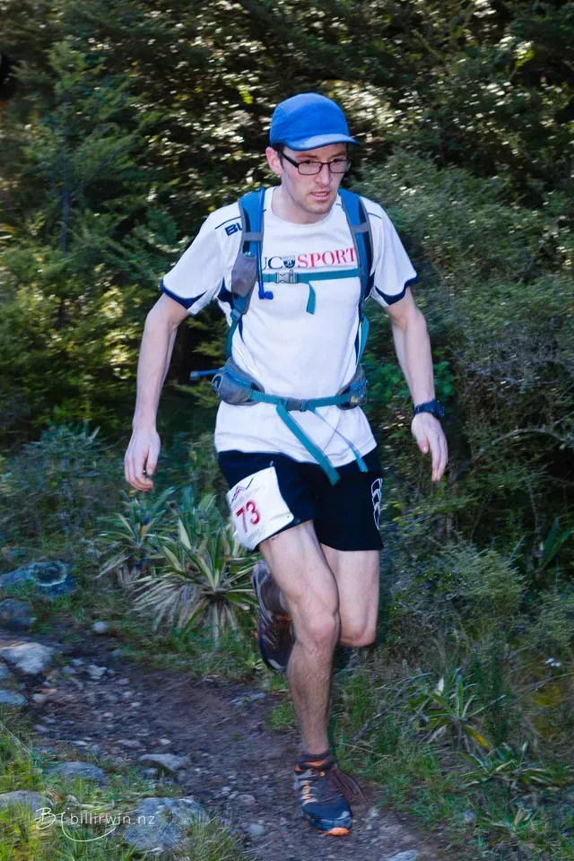 A man is running on a trail in the woods.