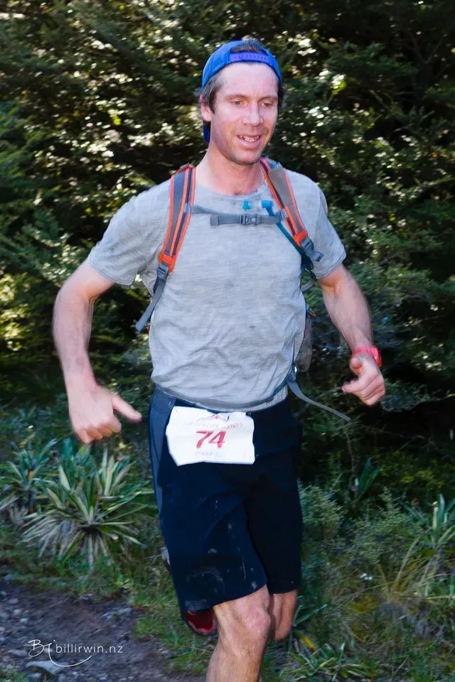 A man wearing a number 74 bib is running in the woods.