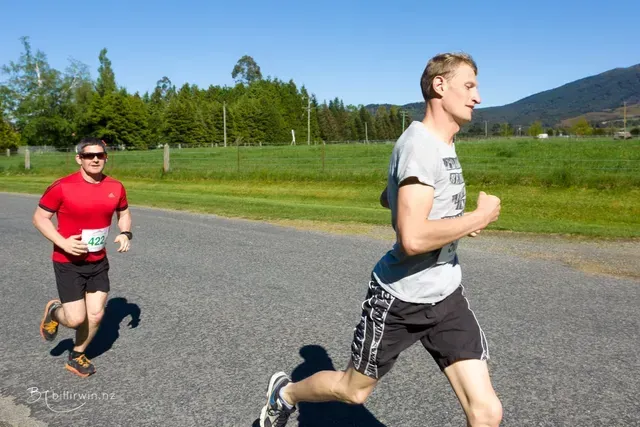 Two men are running on a road and one of them has a number on his shirt