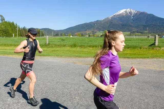 A man and a woman are running on a road with a mountain in the background.