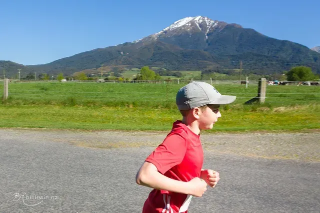 A young boy is running down a road with a mountain in the background.