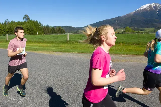 Three people are running on a road with a mountain in the background