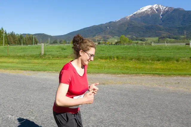 A woman is running down a road with a mountain in the background.