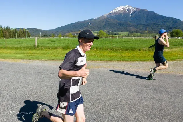 Two people are running on a road with a mountain in the background.