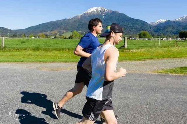 Two men are running on a road with mountains in the background