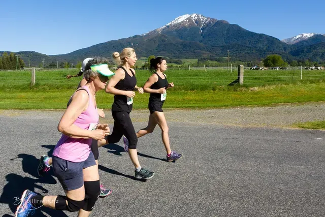 Three women are running on a road with a mountain in the background.