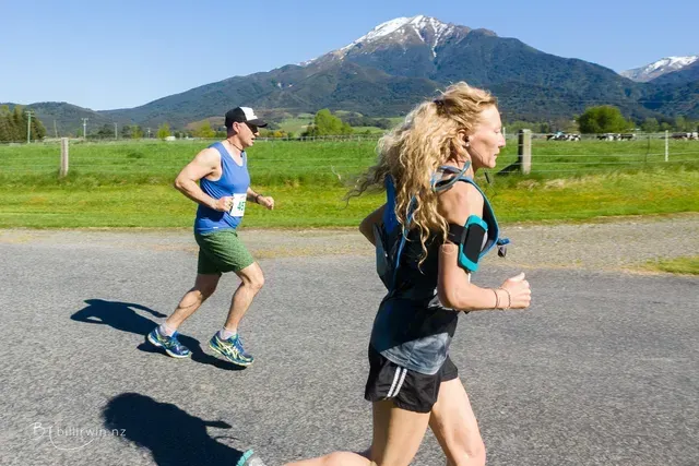 A man and a woman are running on a road with a mountain in the background.