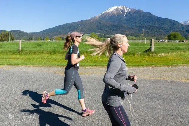 Two women are running on a road with a mountain in the background.