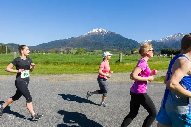 A group of women are running down a road with mountains in the background.