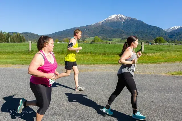 Three people are running on a road with mountains in the background.