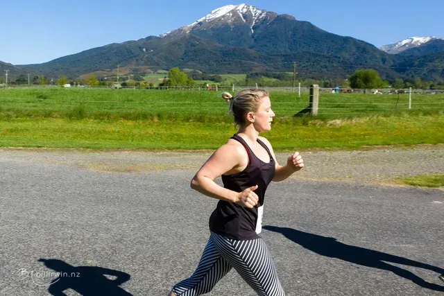 A woman is running on a road in front of a mountain.