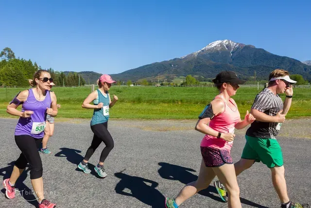 A group of people are running on a road with a mountain in the background.
