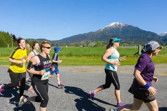 A group of women are running down a road with mountains in the background.