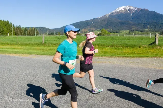 Two women are running on a road with a mountain in the background.