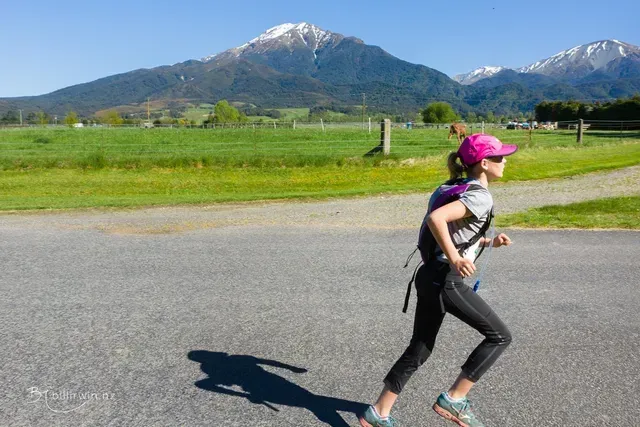 A woman is running down a road with a mountain in the background.