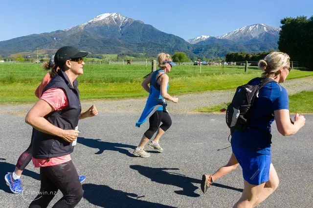 A group of women are running down a road with mountains in the background.