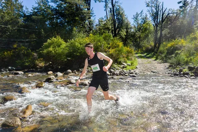 A man is running through a river in the woods.