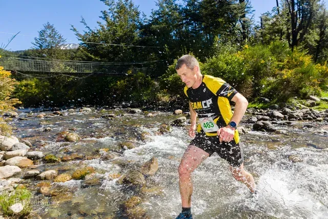 A man in a yellow shirt is running through a river.