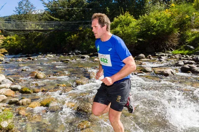 A man in a blue shirt is running through a river.