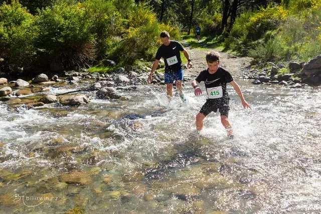 Two people are crossing a river in the woods.