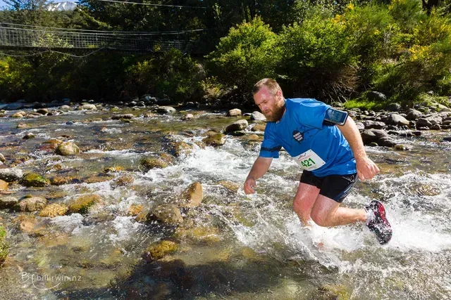 A man in a blue shirt is jumping over a river.