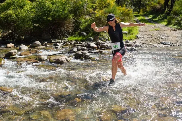A woman is crossing a river with her arms outstretched.