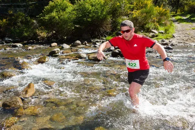 A man in a red shirt is running through a river.