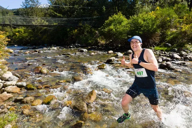 A man is running through a river with a number on his shirt.